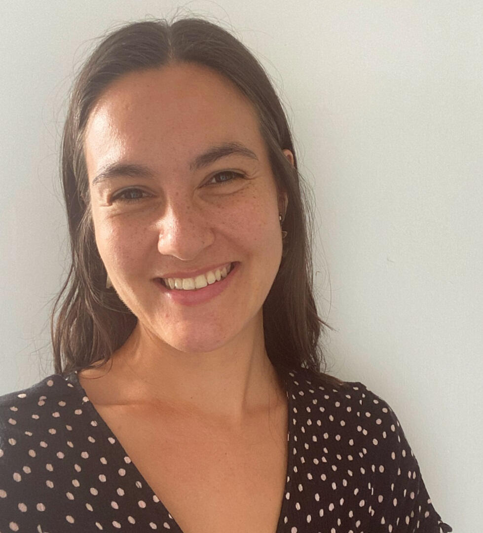 Portrait of Sam smiling in a navy dress with white polka dots on it.